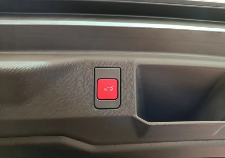 Bouton rouge d'ouverture électrique du coffre sur panneau intérieur noir du Peugeot 5008 gris clair, vue rapprochée.