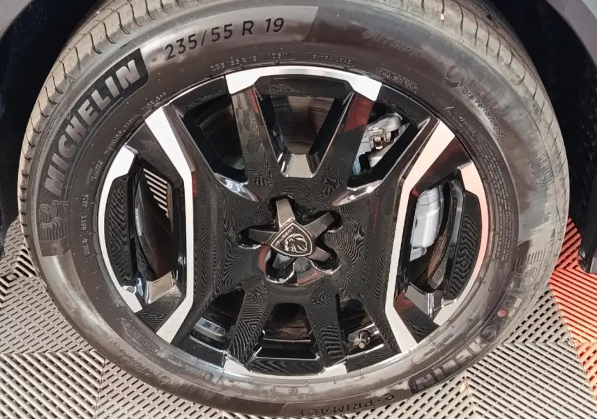 Gros plan sur la roue avant droite du Peugeot 5008 gris clair, avec jante noire et argentée au design moderne.