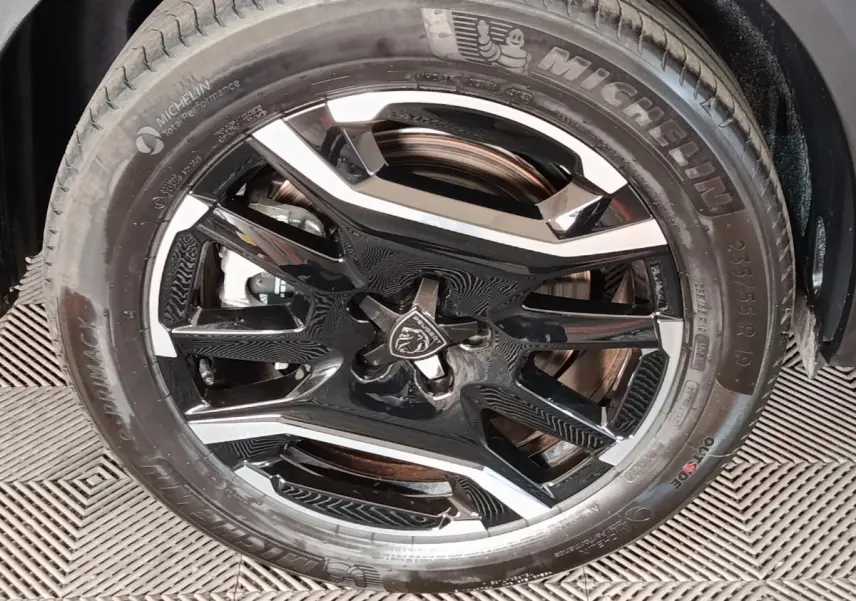 Gros plan sur la roue avant droite d’un Peugeot 5008 gris clair, jante alliage noire et argent avec logo lion central.