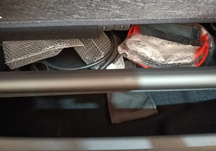 Coffre ouvert du Peugeot 5008 gris clair, montrant câbles et accessoires de recharge rangés sous la tablette.