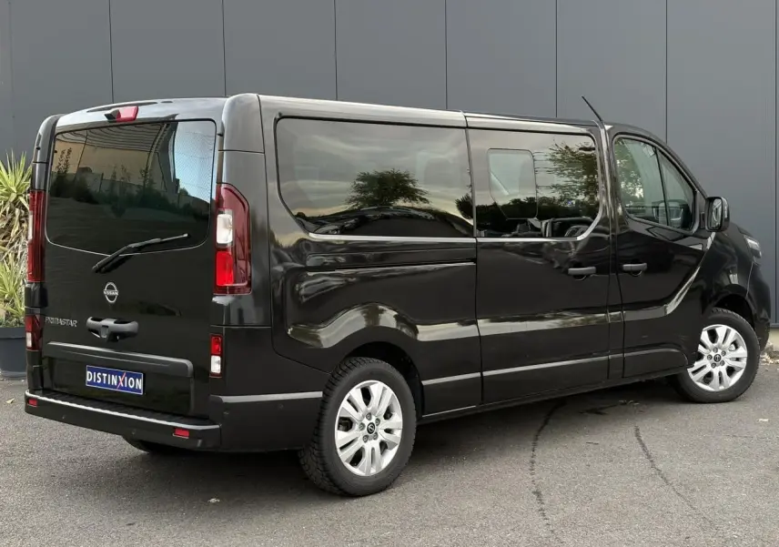 Nissan Primastar Combi noir métal vu en 3/4 arrière droit, hayon vitré et vitres latérales teintées.
