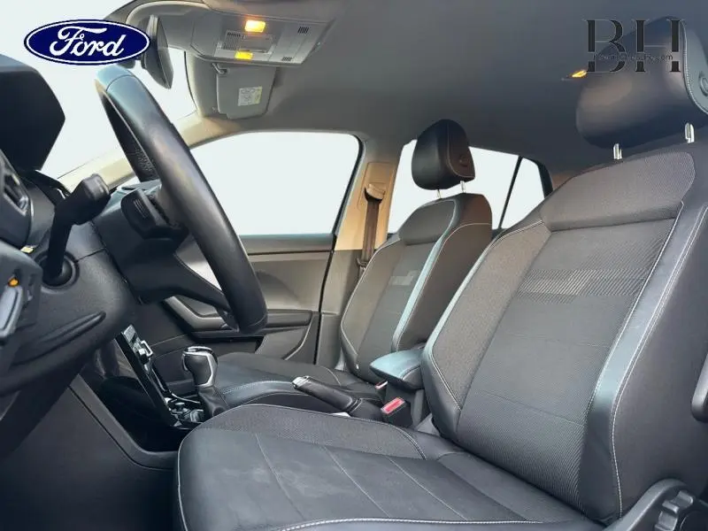 Vue intérieure côté conducteur du Volkswagen T-cross 2022, sièges tissu noir avec surpiqûres grises et volant cuir multifonction.