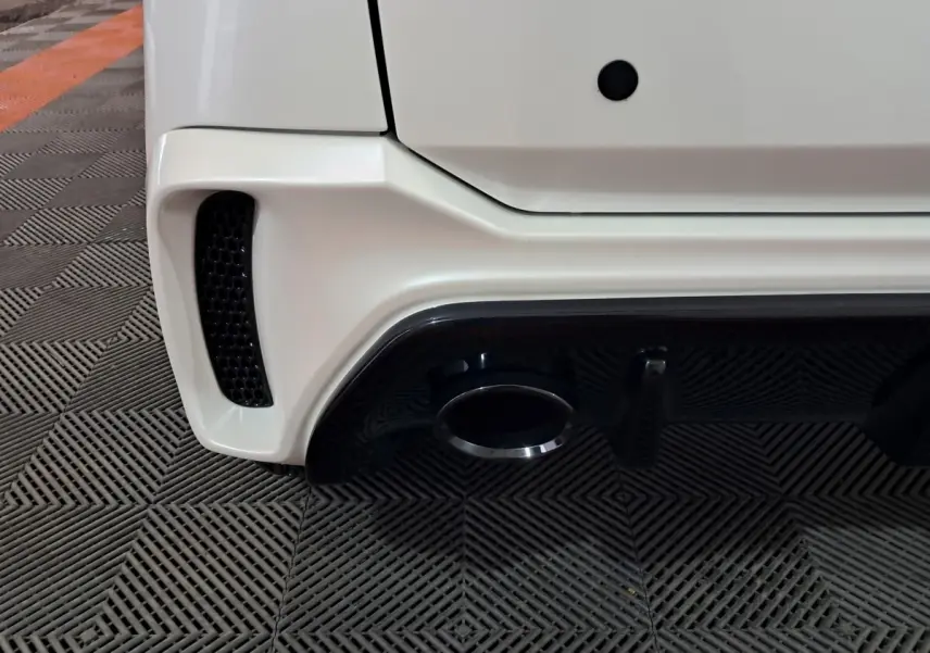 Gros plan sur le bas arrière droit blanc de l'AIXAM AMBITION 0.5 CITY COUPE GTI avec sortie d'échappement et diffuseur noir.