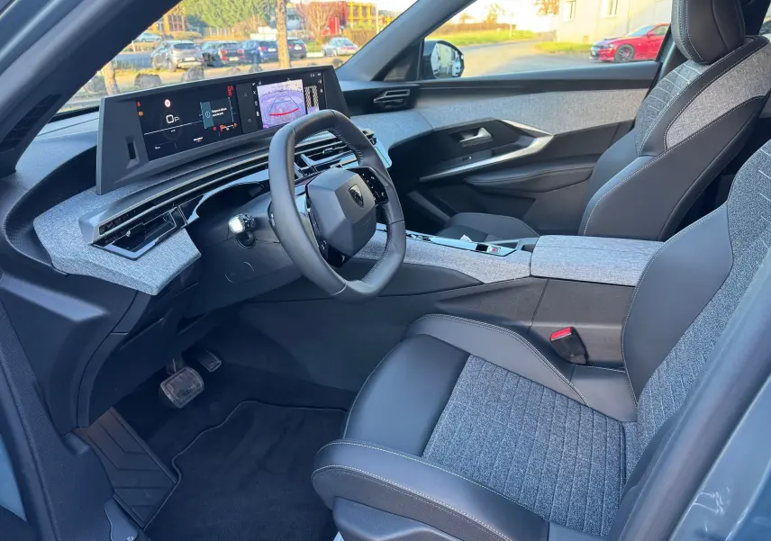 Vue intérieure côté conducteur du Peugeot 3008 Hybrid 136ch Allure 2025, avec sellerie tissu et cuir gris noir et tableau de bord numérique.