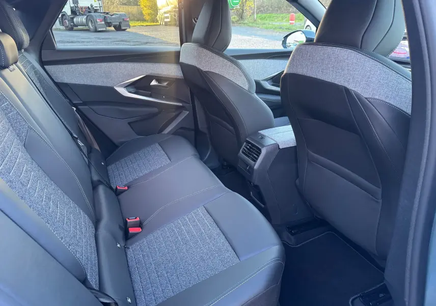 Vue intérieure arrière droite du Peugeot 3008 Hybrid 2025, sièges bi-matière gris et noir avec surpiqûres contrastées.