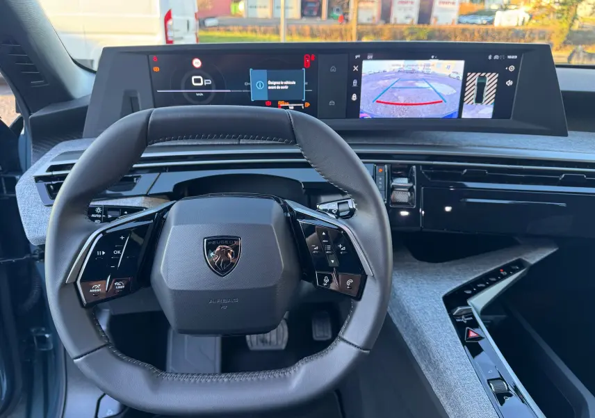 Vue intérieure centrée sur le volant cuir du Peugeot 3008 Hybrid 2025 avec tableau de bord numérique et caméra de recul affichée.