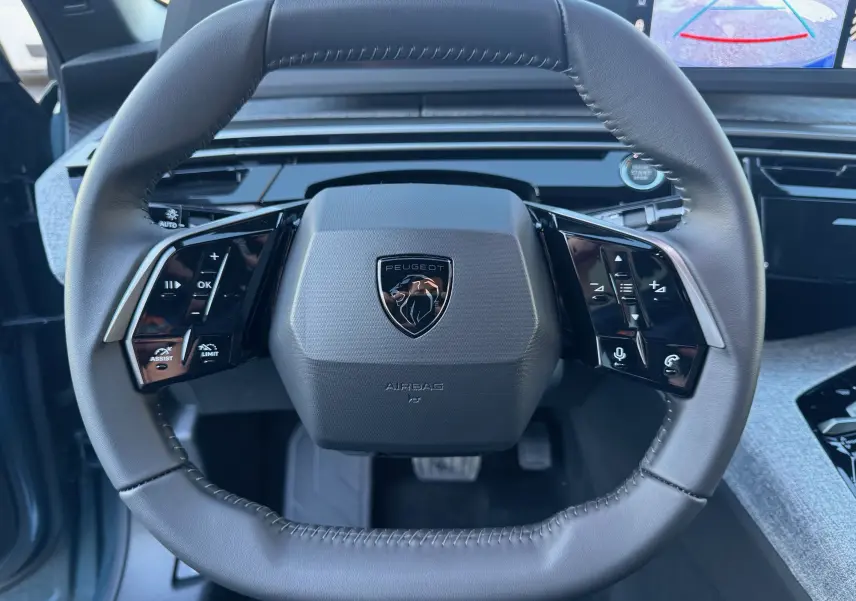 Vue rapprochée du volant cuir noir du Peugeot 3008 Hybrid 2025 avec commandes intégrées et écran de recul visible.