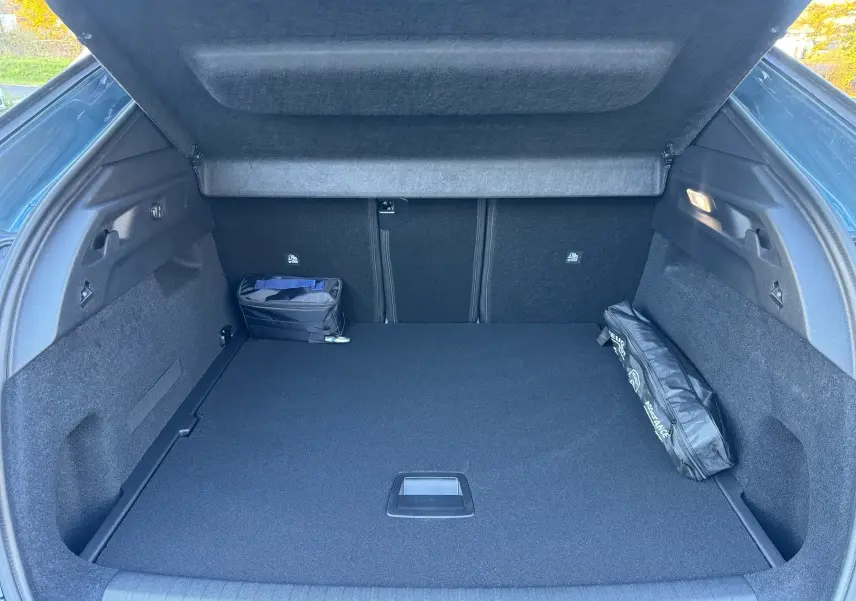 Vue intérieure du coffre ouvert du Peugeot 3008 Hybrid 136ch Allure bleu Nogaro, avec tapis noir et rangement latéral.