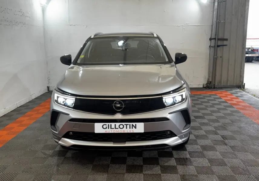 Vue frontale d'un Opel Grandland gris clair avec phares LED allumés dans un garage.