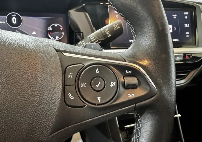 Gros plan sur le volant cuir noir d’un Opel Grandland 2022, avec commandes multifonctions et écran tactile en arrière-plan.