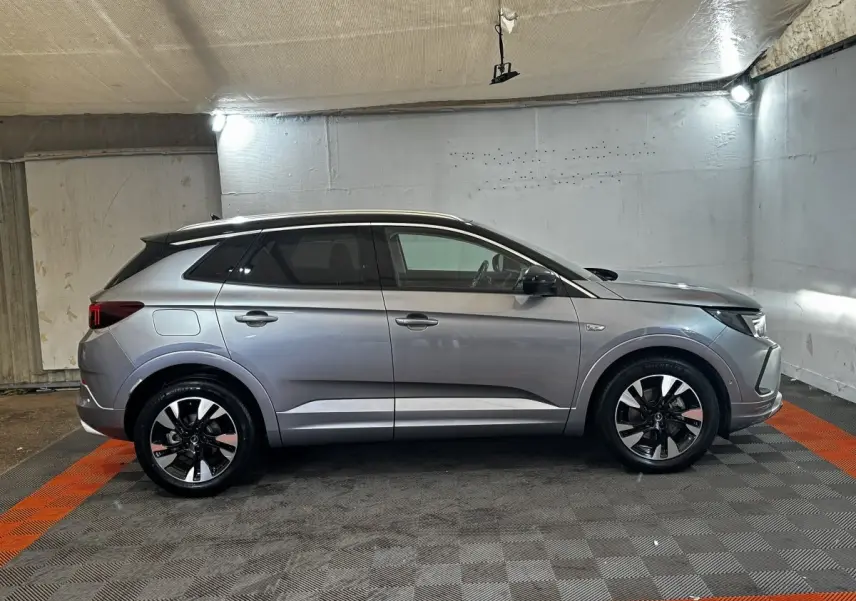 Vue de profil côté gauche d'un Opel Grandland gris clair 2022 avec jantes bicolores et toit noir dans un garage.