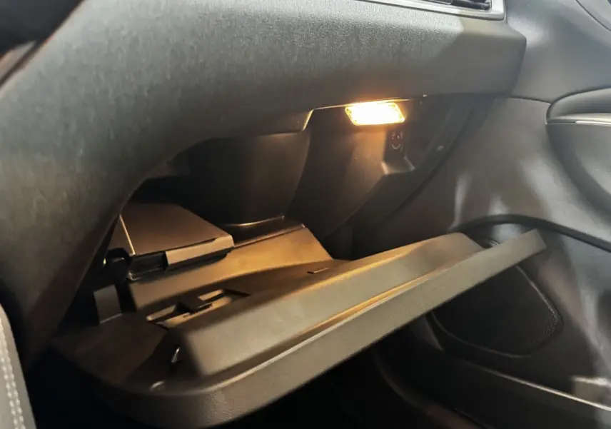 Gros plan sur la boîte à gants ouverte avec éclairage intérieur dans l’habitacle sombre d’un Opel Grandland 2022.