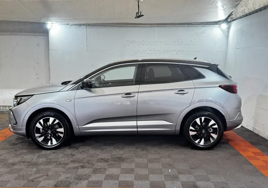 Opel Grandland gris clair vu de profil côté gauche, avec jantes bicolores et toit noir contrastant.