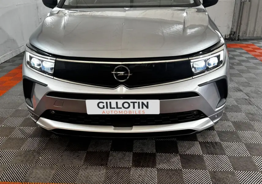 Vue frontale d'un Opel Grandland gris clair avec phares LED allumés et calandre noire brillante.