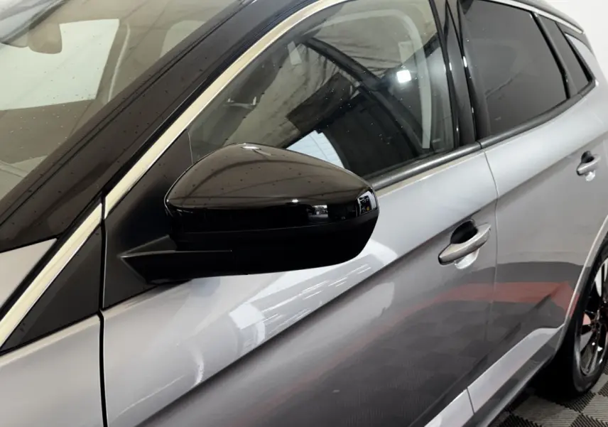 Vue côté gauche rapprochée d’un Opel Grandland gris clair avec rétroviseur noir brillant et poignées de porte assorties.