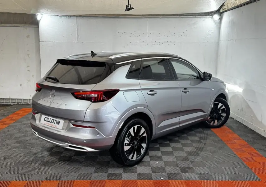 Opel Grandland gris clair, vue 3/4 arrière droit, jantes noires et toit noir contrasté en intérieur.