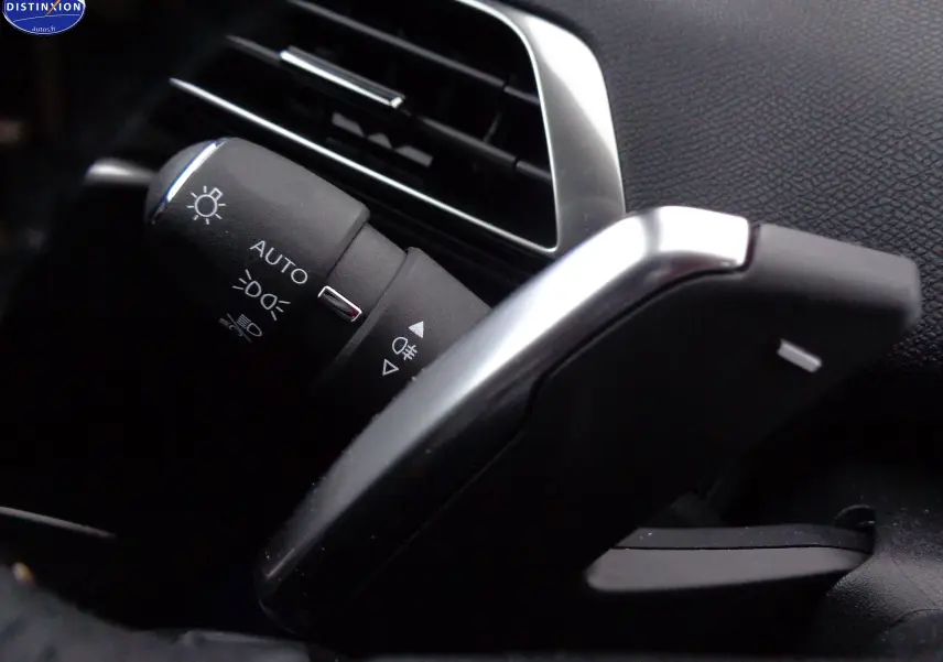 Gros plan sur la commande des phares et lève-vitre argenté dans l'habitacle noir du Peugeot 3008 gris Artense 2023.