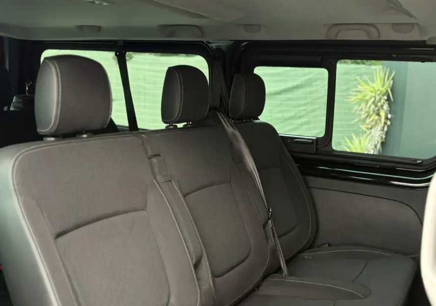 Vue intérieure côté droit sur la deuxième rangée de sièges noirs du Nissan Primastar Combi 2025 avec vitres coulissantes ouvertes.