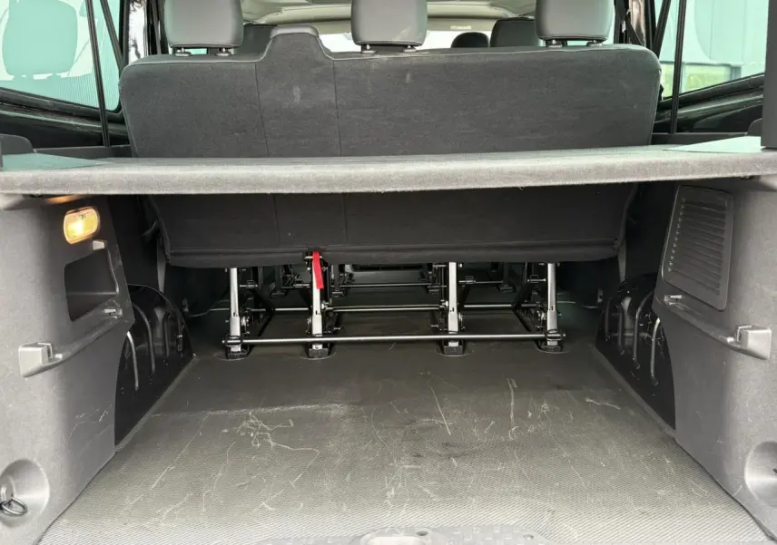 Coffre ouvert du Nissan Primastar Combi noir métal, vue arrière montrant la troisième rangée de sièges et le plancher de chargement.