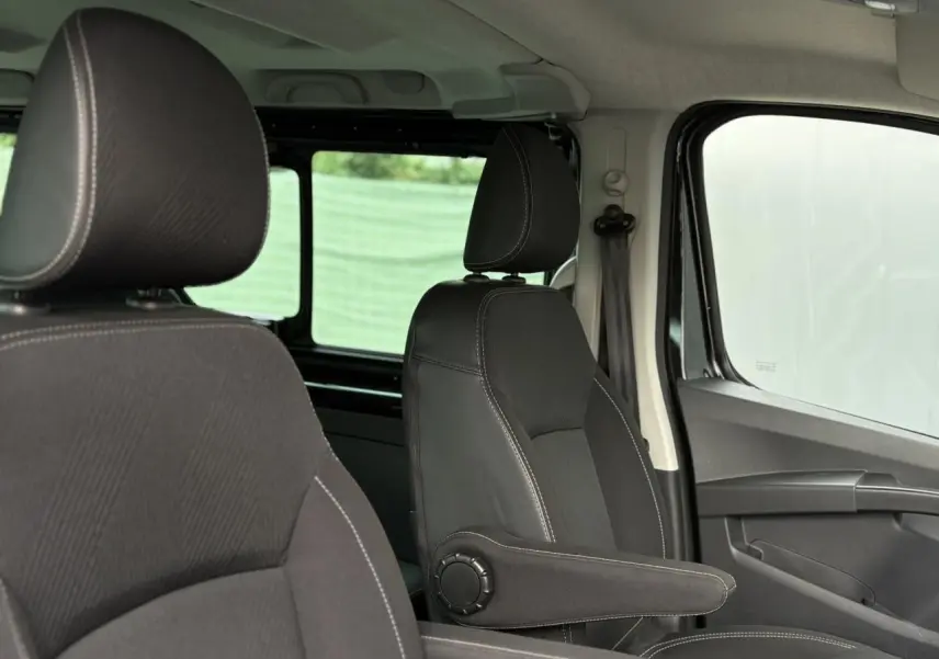 Intérieur du Nissan Primastar Combi 2025, vue côté droit sur sièges noirs avec accoudoirs et vitres latérales.