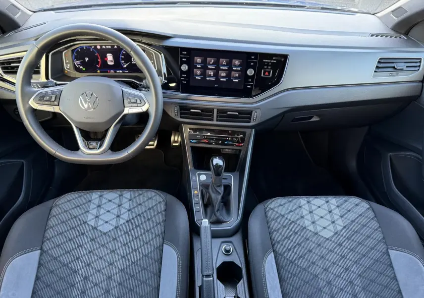 Vue intérieure avant du Volkswagen Taigo 2025, tableau de bord moderne avec écran tactile et sièges tissu gris à motifs géométriques.