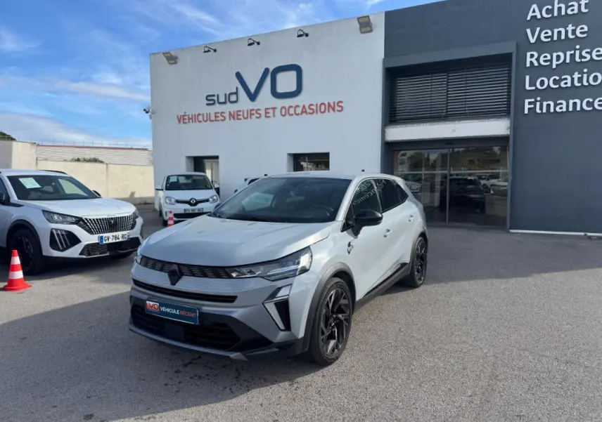 Renault Symbioz gris clair en 3/4 avant droit, avec jantes alliage noires et toit panoramique visible.