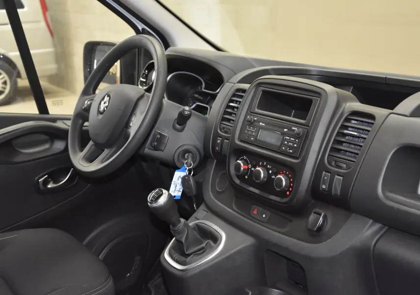 Vue intérieure côté conducteur du Renault Trafic Combi 2.0 DCI 120 avec tableau de bord noir et levier de vitesses manuel.