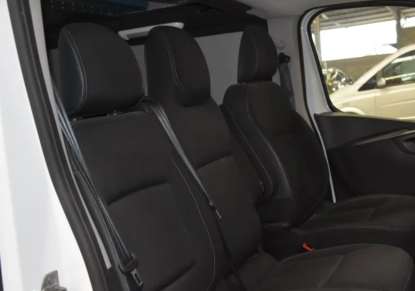 Intérieur du Renault Trafic Combi blanc 2021, vue latérale des sièges avant noirs avec ceintures attachées.