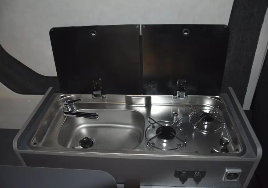 Plan rapproché sur l'évier et le réchaud inox intégrés dans l'aménagement intérieur du Renault Trafic Combi blanc.