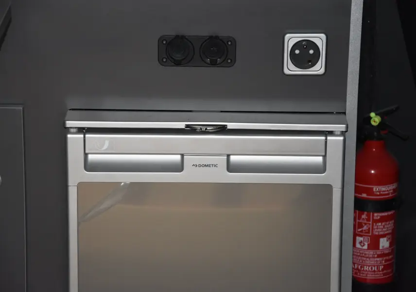 Gros plan sur un réfrigérateur Dometic intégré dans l'aménagement intérieur du Renault Trafic Combi blanc.