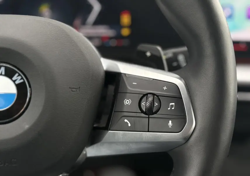 Gros plan sur les commandes multifonctions à droite du volant cuir noir du BMW X1 blanc Mineral 2025.