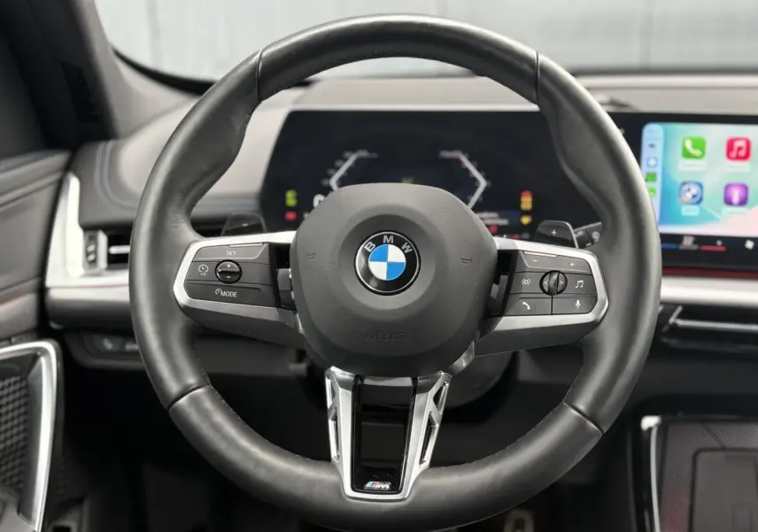 Volant M cuir noir de BMW X1 2025, vue frontale centrée sur les commandes multifonctions et tableau de bord numérique.