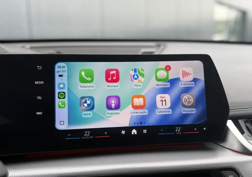 Écran tactile incurvé du tableau de bord du BMW X1 blanc Mineral, affichant l'interface Apple CarPlay.