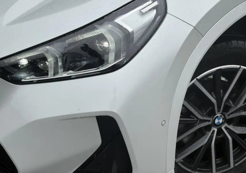 Gros plan sur l'avant droit blanc Mineral du BMW X1 2025 avec projecteur LED et jante alliage 18 pouces style M.