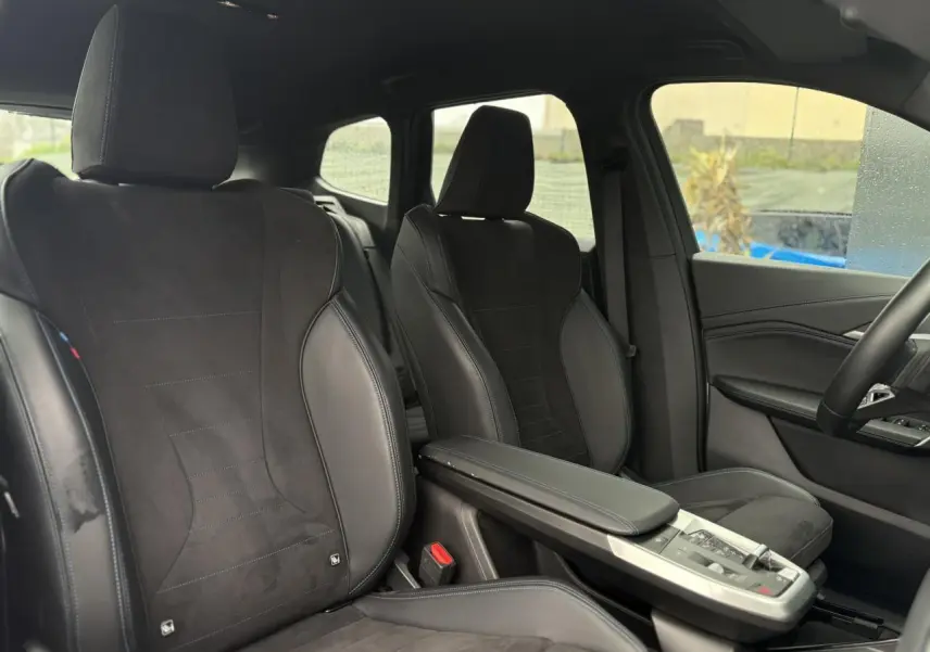 Vue intérieure côté droit montrant les sièges avant sport en Alcantara noir avec surpiqûres bleues du BMW X1 2025.