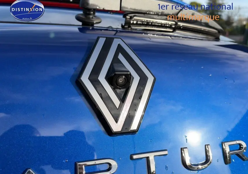 Gros plan sur le logo Renault et la calandre d’un Captur bleu iron 2025 avec caméra de recul intégrée.