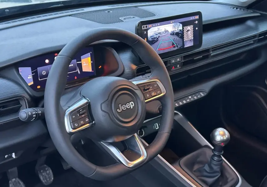 Vue intérieure centrée sur le volant Jeep et la console avec levier de vitesse manuelle et écran multimédia affichant la caméra de recul.