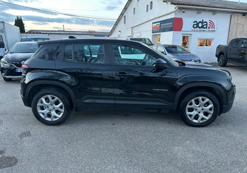 Vue de profil côté gauche d'un Jeep Avenger noir 2025 avec jantes alliage 17 pouces, garé devant un bâtiment commercial.