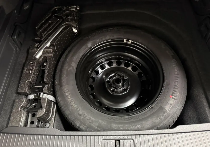 Gros plan sur la roue de secours noire et le cric dans le coffre d’une Volkswagen Passat SW 2024 gris pyrite.