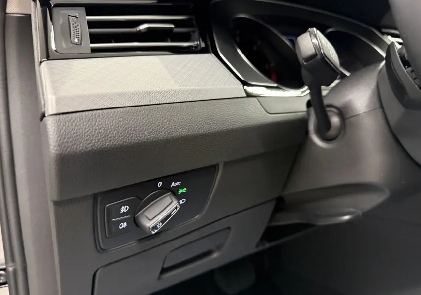 Gros plan sur le bouton de commande des phares à gauche du volant dans l’habitacle gris d’une Volkswagen Passat SW 2024.