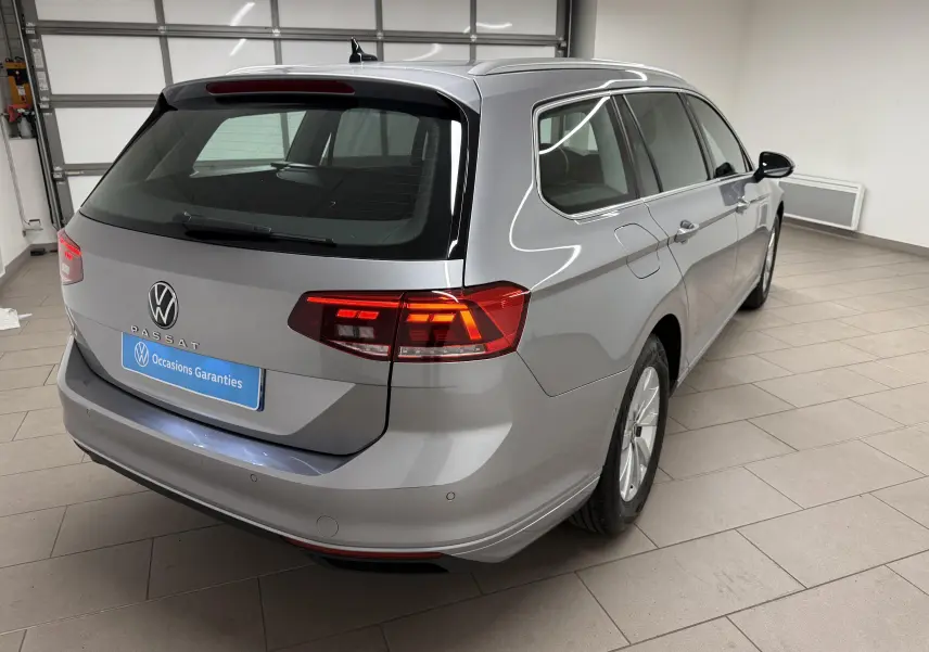 Vue 3/4 arrière droite d'une Volkswagen Passat SW 2024 gris pyrite avec feux arrière allumés dans un garage.