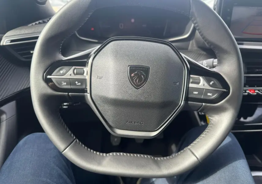 Vue rapprochée du volant cuir noir du Peugeot 2008 2024 avec commandes intégrées et logo central.