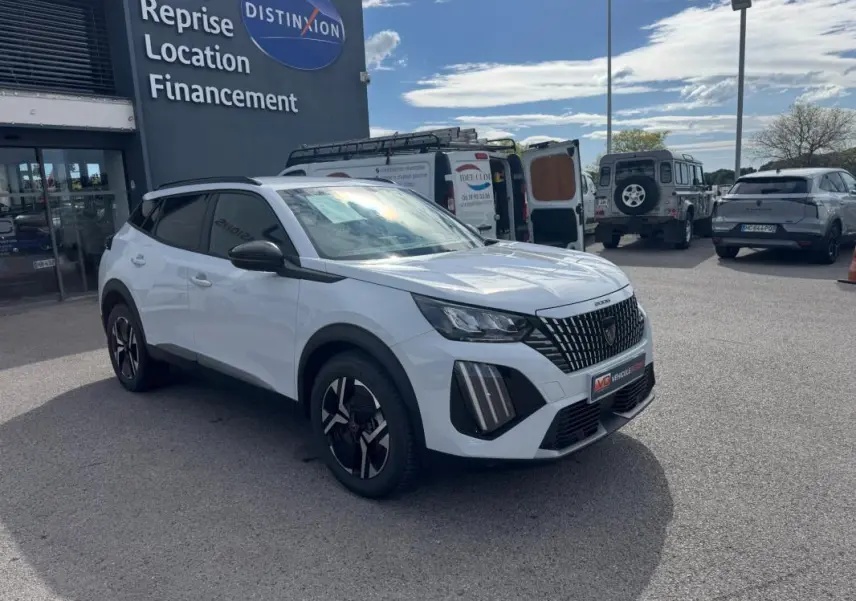 Peugeot 2008 blanc en 3/4 avant droit, avec barres de toit noires et jantes alliage 17 pouces visibles.