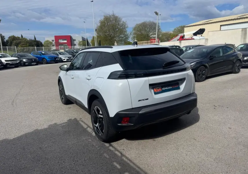 Vue 3/4 arrière droite d’un Peugeot 2008 blanc avec barres de toit et jantes alliage 17 pouces, stationné en extérieur.