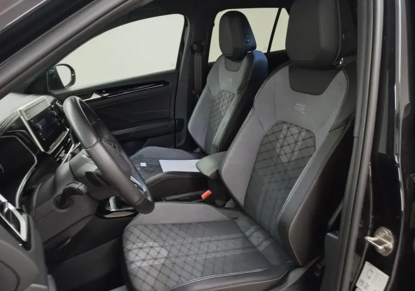 Vue intérieure côté conducteur du Volkswagen T-Roc 1.5 TSI R-Line 2025, sièges sport en cuir et alcantara noirs avec surpiqûres grises.