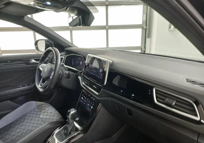 Vue intérieure côté conducteur du Volkswagen T-Roc 1.5 TSI 2025, tableau de bord noir avec écran tactile central.