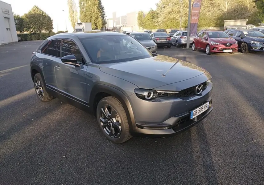 Vue 3/4 avant d'une Mazda MX-30 gris électrique, avec ses phares ronds caractéristiques et ses jantes noires distinctives.