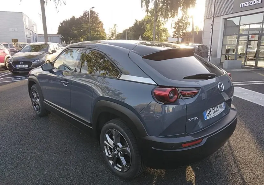 Vue 3/4 arrière droite d'un Mazda MX-30 gris électrique 2021 avec vitres teintées et jantes distinctives.