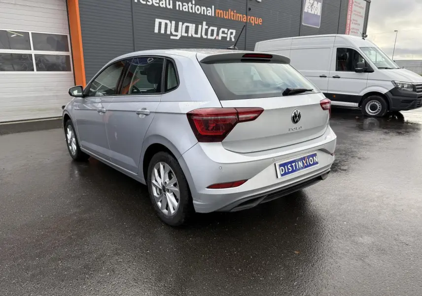 Volkswagen Polo 2025 argent métallisé vue 3/4 arrière droit sur sol mouillé devant un garage.
