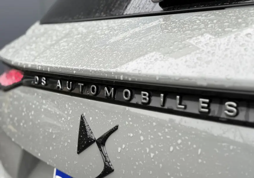 Gros plan sur l'arrière gris laqué du DS7 2024 avec logo DS et lettrage DS Automobiles sous la pluie.